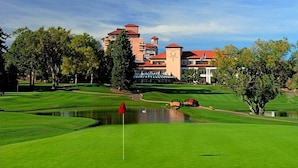 A golf course with a pond, trees, and a building with a red roof in the background.