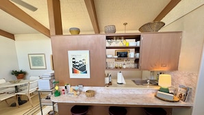 A compact kitchen with a marble countertop, wooden cabinets, and a hanging light fixture.