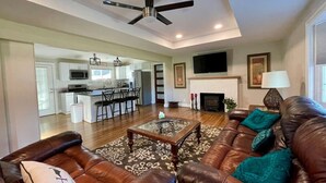 A spacious living room with a brown leather sofa, a glass coffee table, and a fireplace. - Urban Retreat near Wake Forest & Downtown WS (Winston-Salem)