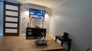 A living room with a wooden table, a TV mounted on the wall, and a black entertainment unit. - Urban Retreat near Wake Forest & Downtown WS (Winston-Salem)