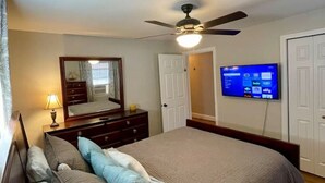 A bedroom with a bed, a ceiling fan, a TV mounted on the wall, and a dresser. - Urban Retreat near Wake Forest & Downtown WS (Winston-Salem)