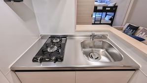 A modern kitchen with a gas stove, stainless steel sink, and wooden cabinets. - MP Hotel Hakata (Fukuoka)