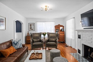 A living room with a sofa, two leather chairs, a coffee table, a fireplace, a television, and a bookshelf. - The Rock Haus - Hot Tub & Fire Pit (Fredericksburg)