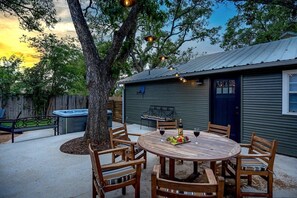 A wooden outdoor dining table with chairs, a hot tub, and a barbecue grill in a backyard setting. - The Rock Haus - Hot Tub & Fire Pit (Fredericksburg)
