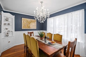 A dining room with a wooden table, chairs, a chandelier, a potted plant, and a painting on the wall. - The Rock Haus - Hot Tub & Fire Pit (Fredericksburg)