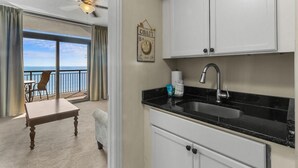 A room with a balcony, a dining table, a kitchen with a sink, and a ceiling fan. - Relax and Unwind: Oceanfront 1 Bdrm Condo (North Myrtle Beach)