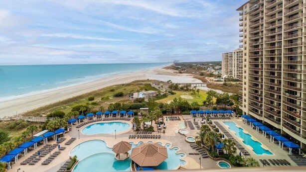 Ein Resort mit mehreren Schwimmbecken, Blick auf den Strand und einem großzügigen Gebäude mit Balkonen.