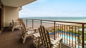 Ein Balkon mit Adirondack-Stühlen mit Blick auf einen Strand und einen Poolbereich.