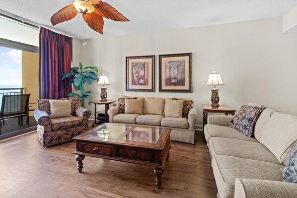 Ein Wohnzimmer mit Couchtisch aus Holz, zwei Sofas, einem Sessel und einer großen Pflanze.