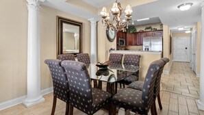 A dining area with a glass table and patterned chairs, a chandelier, and a kitchen in the background. - Beachfront Beauty 2BR 2BA Condo with Kitchen (North Myrtle Beach)