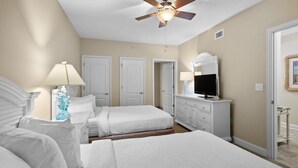 Une chambre avec deux lits, un ventilateur de plafond, une télévision et une commode.