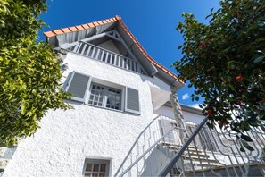 Un edificio blanco con techo de tejas rojas, un balcón y una escalera.