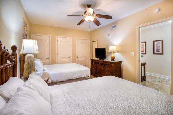 Une chambre d’hôtel avec deux lits, un ventilateur de plafond, une télévision, une commode et une porte.