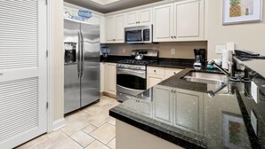 A kitchen with white cabinets, stainless steel appliances, a granite countertop, and a tiled floor. - Sun, Sand and Sea Views 3 Bdrm Condo with Balcony (North Myrtle Beach)