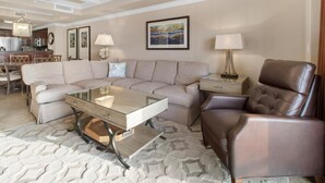 A living room with a sectional sofa, a glass coffee table, a leather armchair, and a dining area with a chandelier. - Unparalleled Luxury: 3 Bdrm Condo with Whirlpool (North Myrtle Beach)