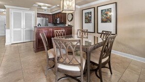 A dining area with a round table and chairs, a kitchen in the background, and artwork on the walls. - Unparalleled Luxury: 3 Bdrm Condo with Whirlpool (North Myrtle Beach)