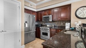 A kitchen with stainless steel appliances, dark wooden cabinets, a large wall clock, and a tiled backsplash. - Unparalleled Luxury: 3 Bdrm Condo with Whirlpool (North Myrtle Beach)
