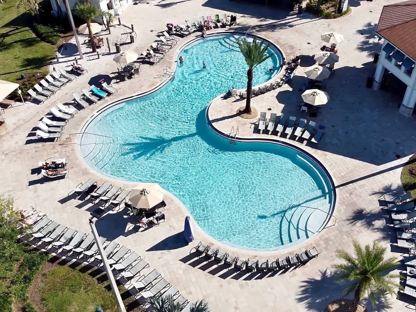 A large, uniquely shaped swimming pool surrounded by sun loungers and umbrellas, with a building in the background.