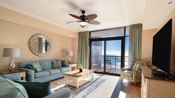 Ein geräumiges Wohnzimmer mit einer Couch, einem Couchtisch und einem Fernseher. Es gibt einen Balkon mit Meerblick.