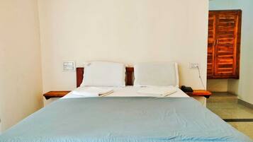 Quarto de hotel padrão com uma cama, duas mesas de cabeceira, um guarda-roupa de madeira e uma tomada na parede.