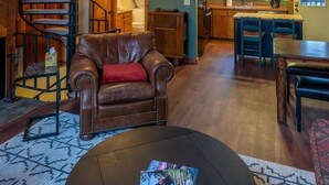 En rummelig opholdsstue med en spiraltrappe, en lædersofa, et spisebord og et køkken i baggrunden.