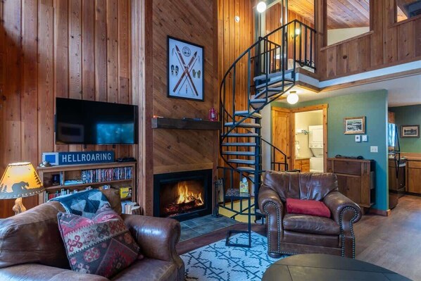 Interior de madera con chimenea, mobiliario de cuero, televisor y una escalera en espiral.