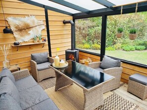 Relax in a sheltered outdoor space with a glass-enclosed design, featuring two cushioned sofas and a coffee table.