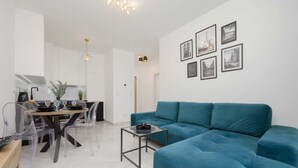 Een moderne woonkamer met een blauwgroene bank, een eethoek met een tafel en stoelen, en een keuken op de achtergrond.