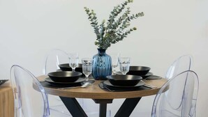 Een ronde eettafel met een blauwe vaas met groene bladeren, zwarte borden en helder glaswerk.