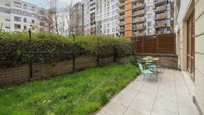 A residential building with a small garden area, outdoor seating, and a brick wall. - Elegant Apartment in Wola | Terrace from Two Rooms (Warszawa)
