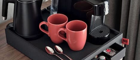 A black tray with a coffee maker, two red mugs, a black kettle, and a spoon set on a textured mat.