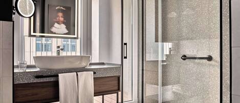 A modern bathroom with a large mirror, a round sink, a glass shower enclosure, and a towel rack.