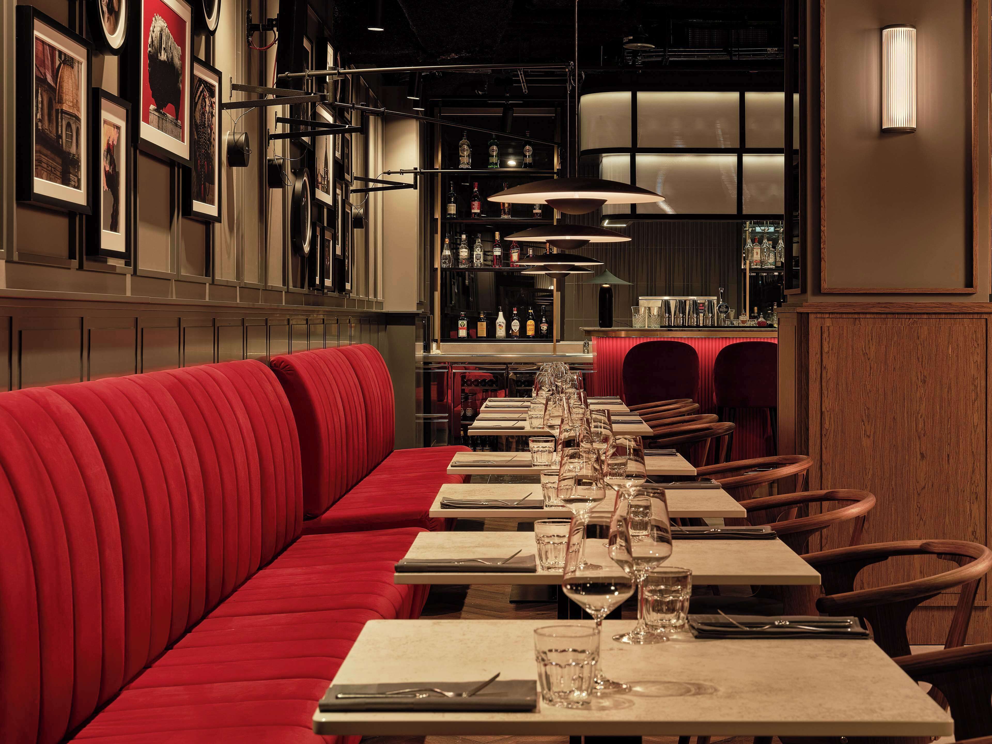 Un restaurante con cabinas tapizadas en rojo, mesas ordenadas con copas de vino y un área de bar al fondo.