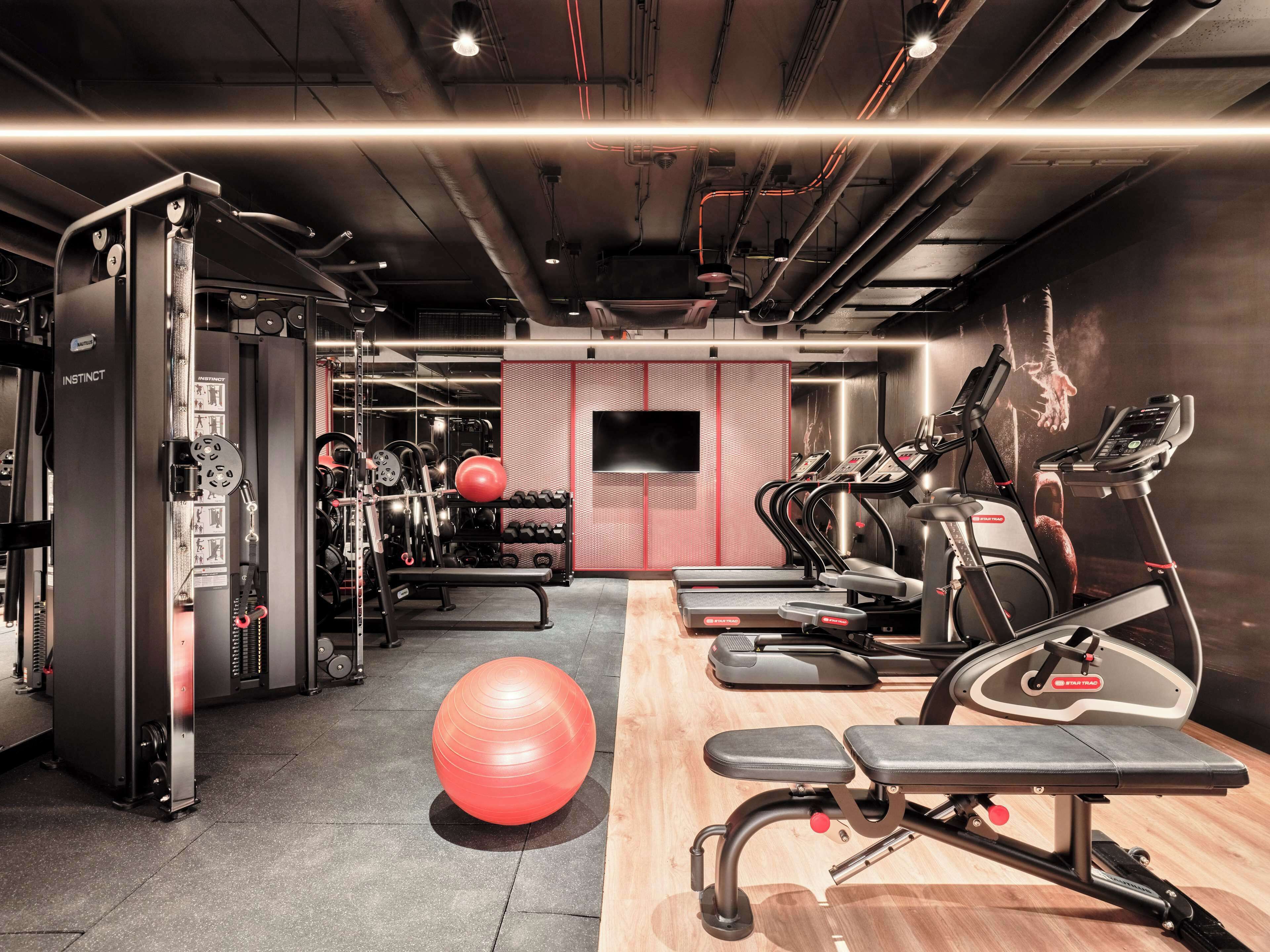Un gimnasio con equipamiento de ejercicio, una pelota roja grande y un banco de madera.