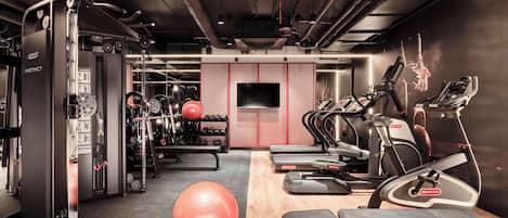 Un gimnasio con equipamiento de ejercicio, una pelota roja grande y un banco de madera.