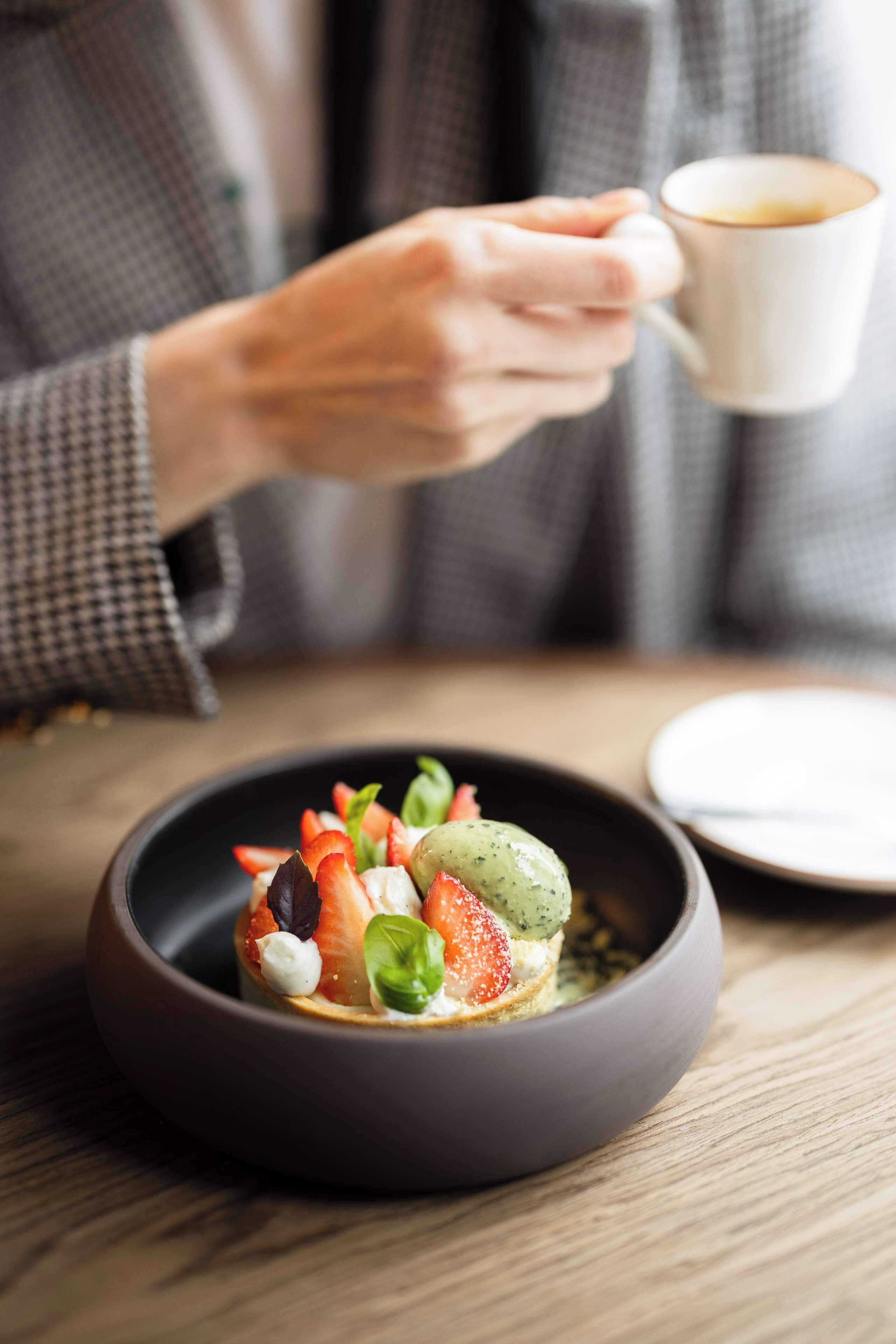 Una persona sosteniendo una taza de café, con un plato de comida en primer plano.