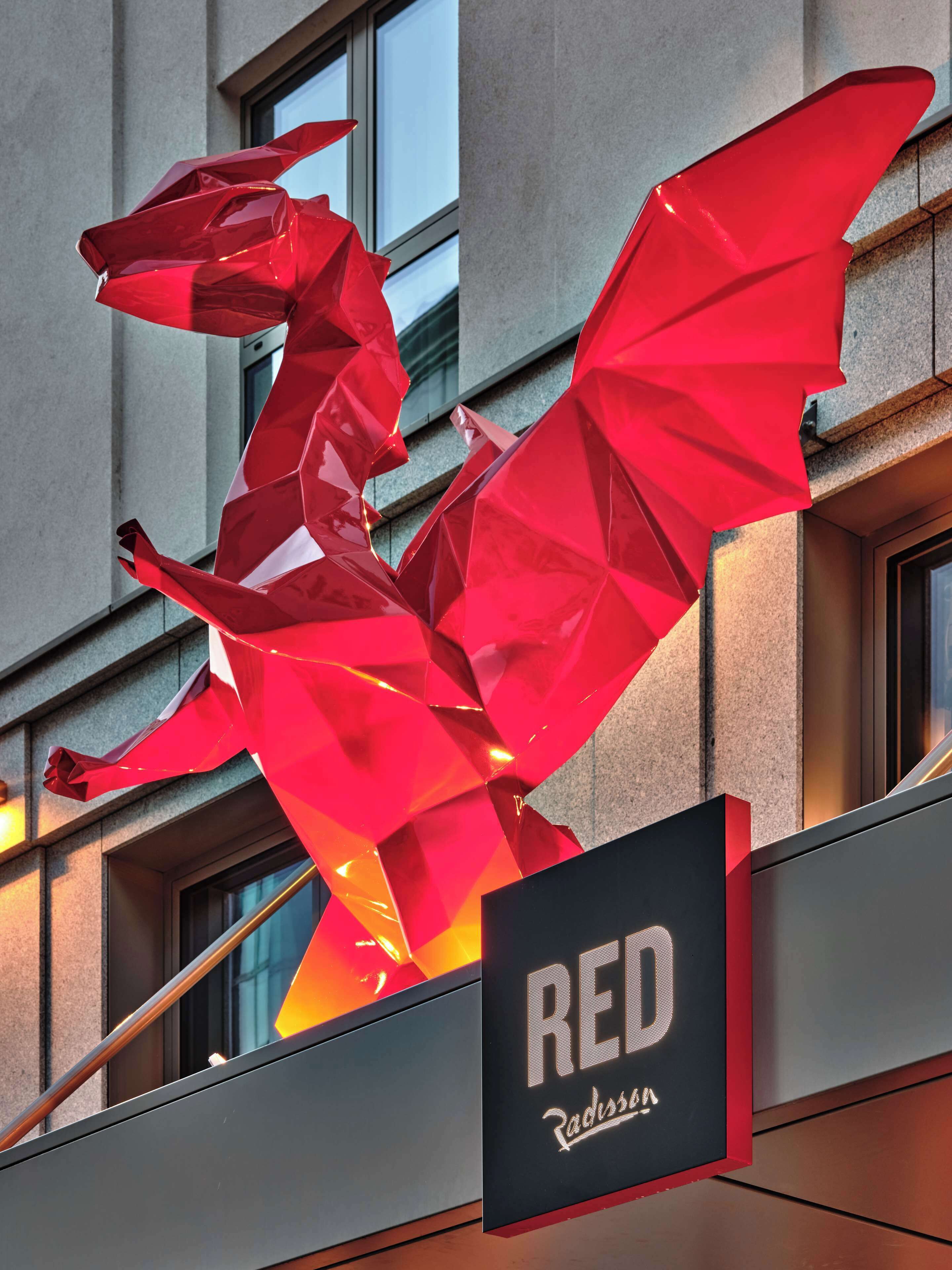 A red dragon sculpture in front of a building with a sign that reads "RED Radisson."