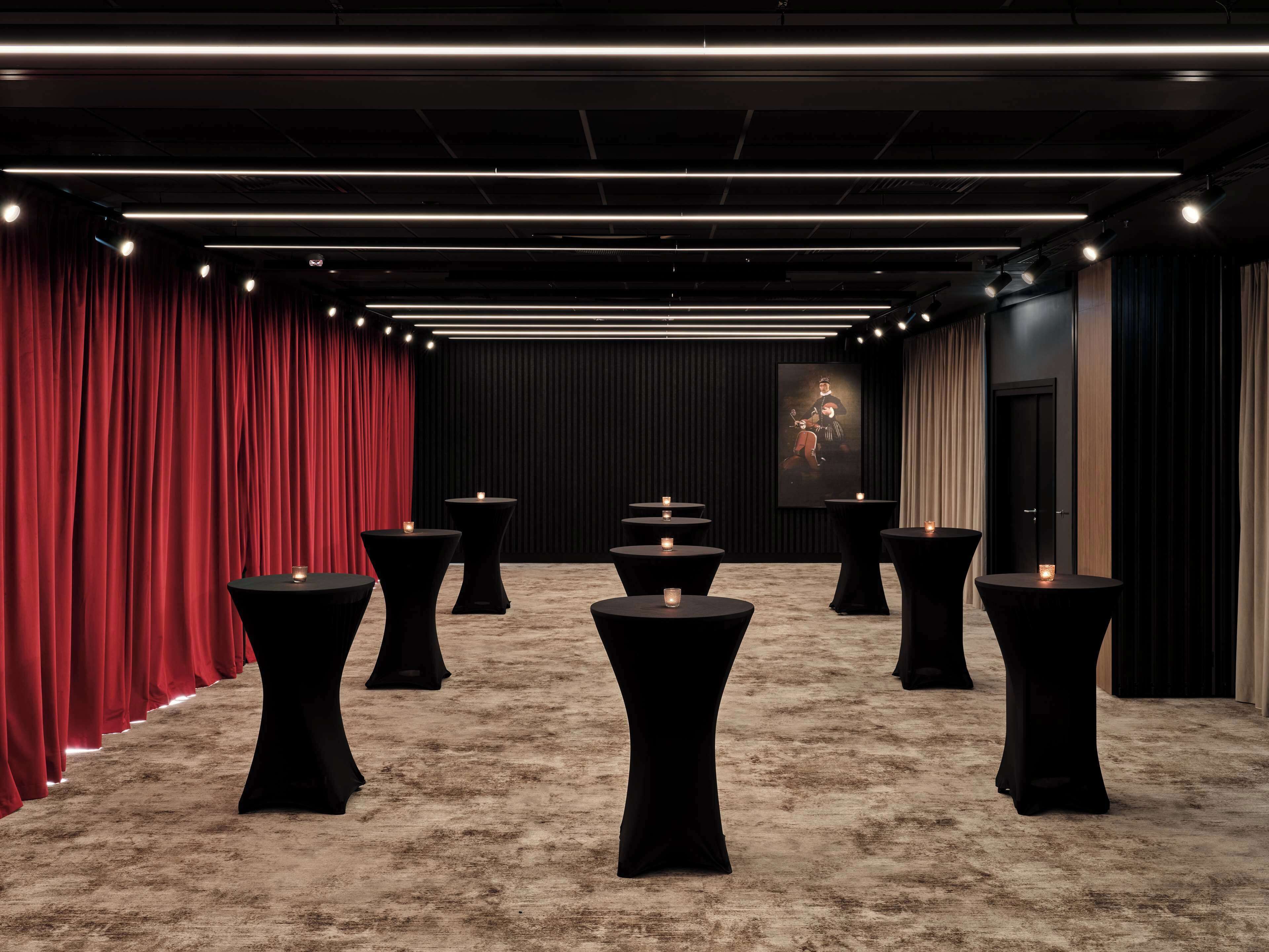 Un salón de conferencias con un escenario, cortinas rojas y varias mesas con velas.