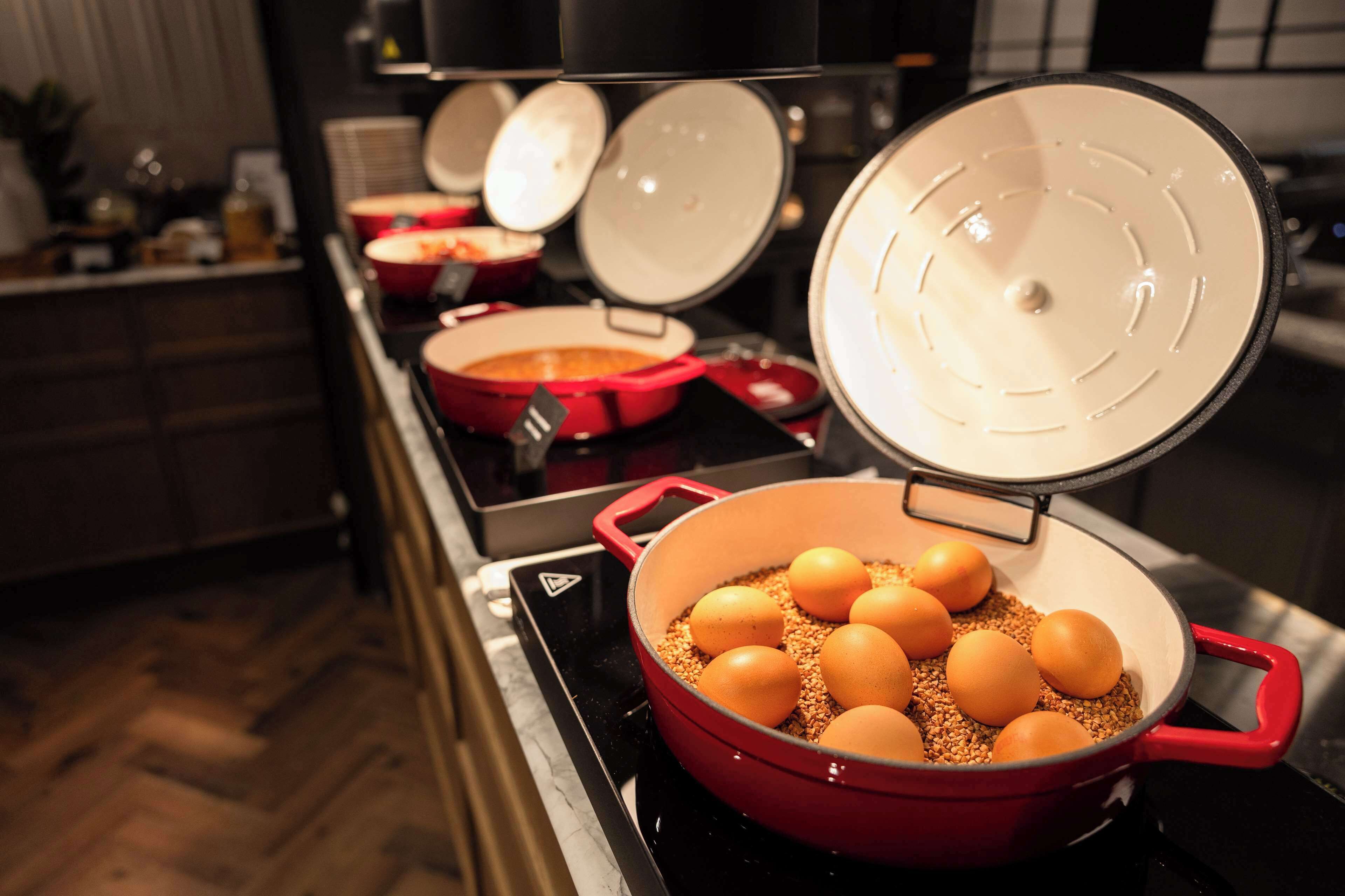 A kitchen with a red pot containing eggs and grains on a stove.
