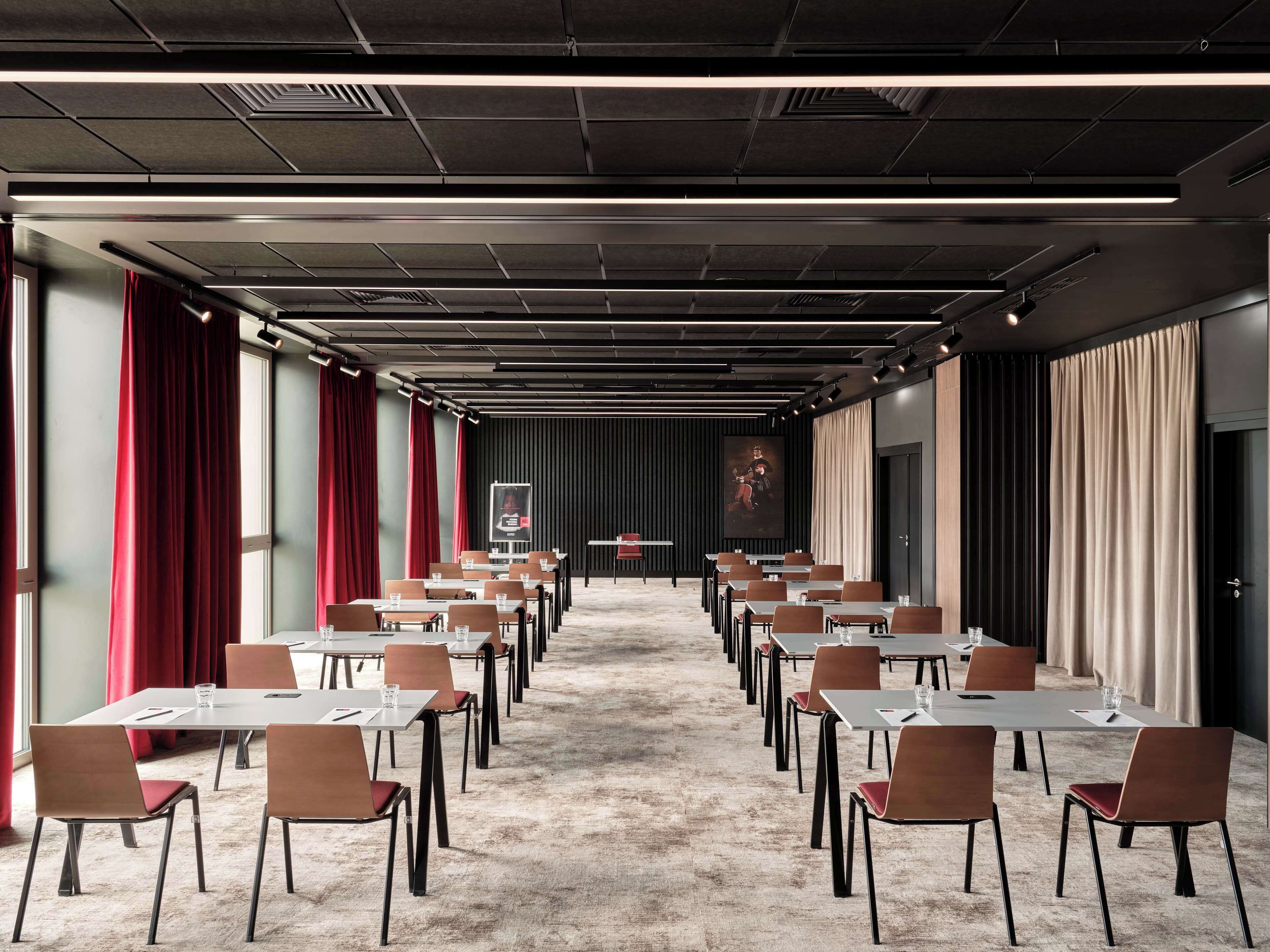 A conference room with rows of tables and chairs, a stage with a podium, and a large painting on the back wall.