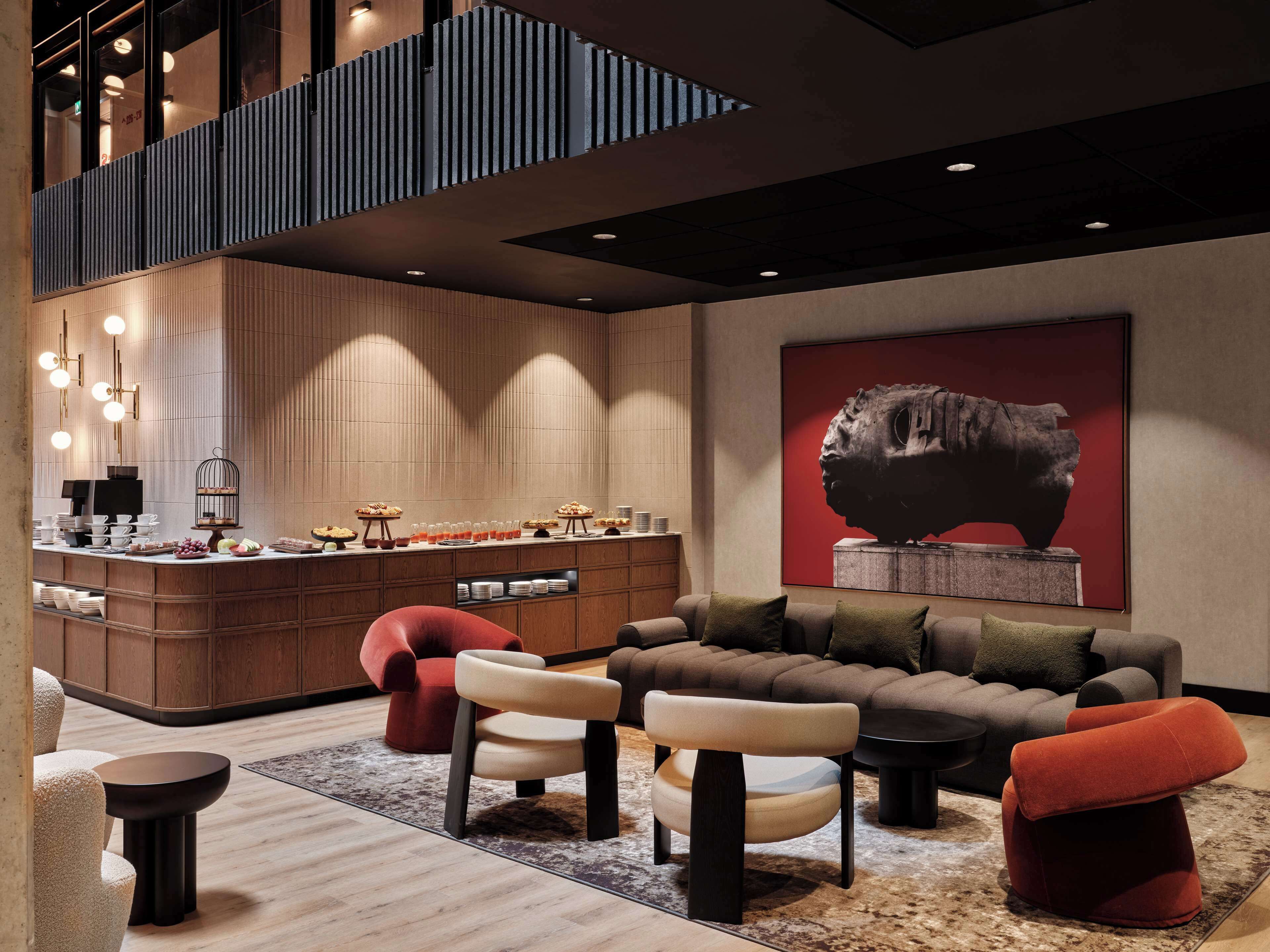 A modern hotel lobby with a central seating area, a bar, and a high ceiling with recessed lighting.