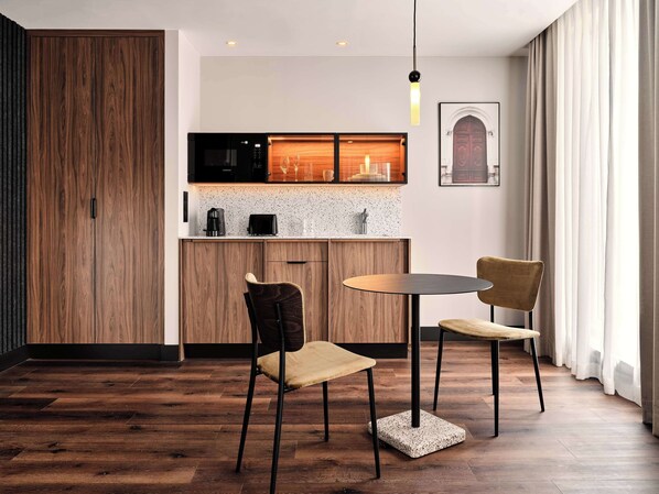 A modern kitchen with wooden cabinets, a microwave, and a coffee maker. There is a dining area with two chairs and a table. - Radisson RED Hotel & Radisson RED Apartments, Kraków (Kraków)