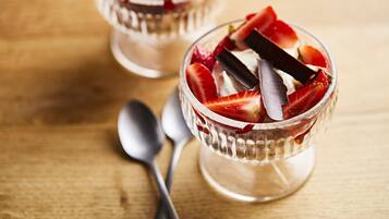 Duas taças de vidro transparentes com morangos e chocolate sobre uma mesa de madeira.