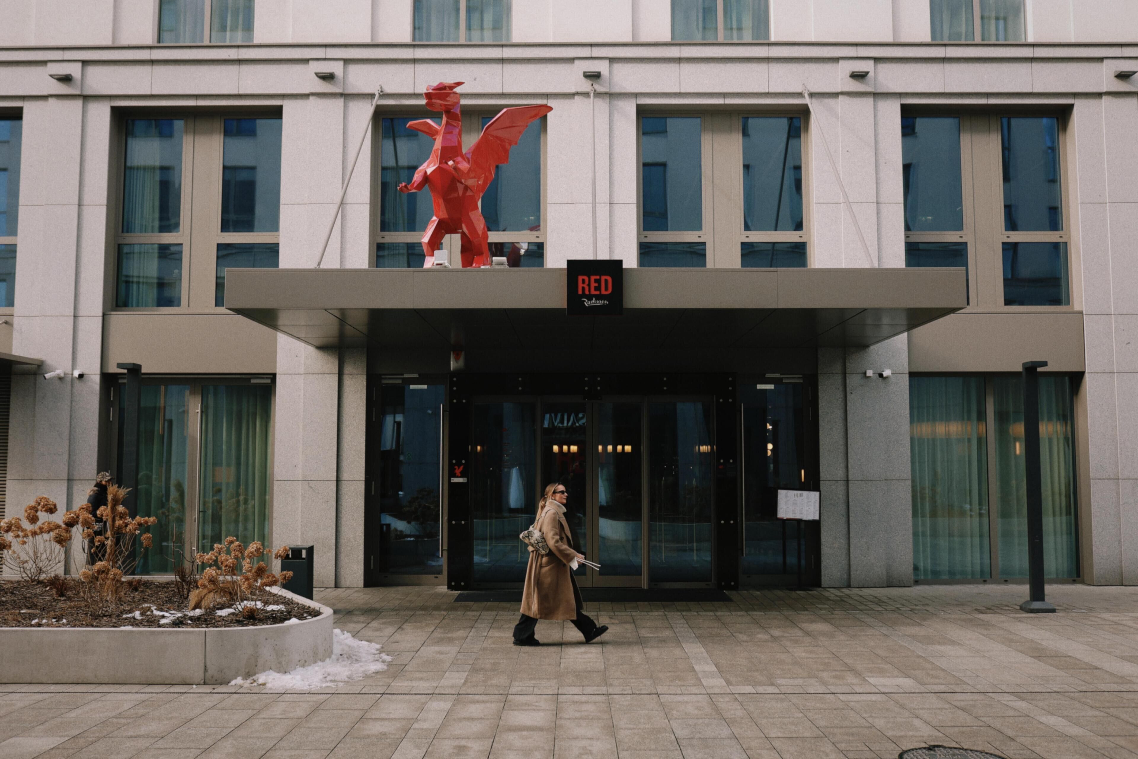 Un edificio con una estatua de dragón rojo, un cartel que dice 'RED' y una persona caminando al frente.