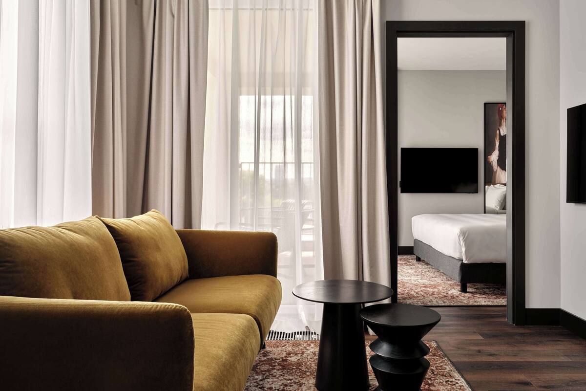 Una habitación de hotel moderna con un sofá, una mesita redonda negra y una cama con cabecera blanca.