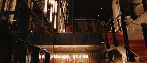 Un hall de hotel de varios niveles con una escalera central, una recepción y zonas de estar modernas.