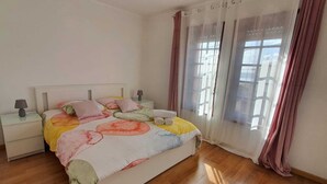 Ein Schlafzimmer mit einem Bett, zwei Nachttischen, einer Lampe und einem Fenster mit Vorhängen.