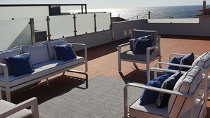 Eine Dachterrasse mit weißer Gartenmöblierung, darunter Sofas und Sessel, auf einem gefliesten Boden.