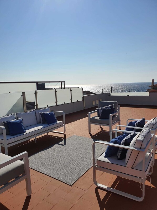 Una terraza en la azotea con mobiliario exterior blanco, incluyendo sofás y sillones, dispuesto sobre un suelo de baldosas.