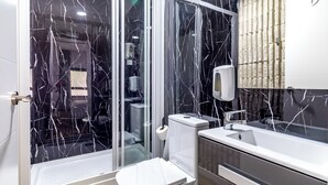 A bathroom with a glass shower enclosure, a toilet, a sink, and a mirror. - AYZ Princesa - Auto check-in property (Madrid)